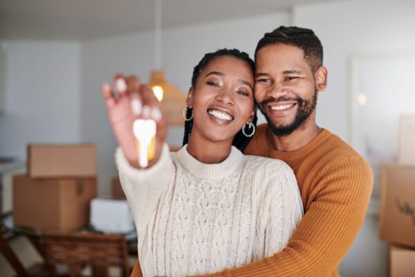 shot of a young couple hugging while showing their new house keys at home - Home - Ayokunle Homes